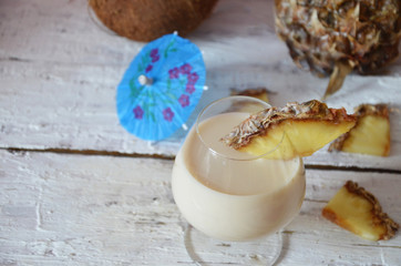 Traditional caribbean cocktail pina colada in a glasses on a blue background. Cocktail or juice with pineapple and coconut on the background in a  glass on a pink, white wooden with an umbrella