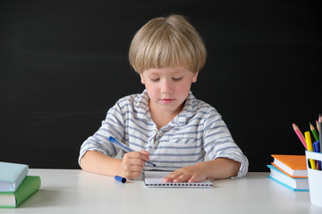 Back to school. Cute little boy sitting at the table on blackboard backgrpund. Child from elementary school. Education concept.