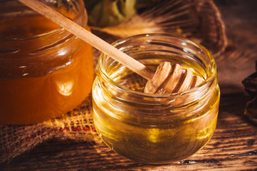 Fresh summer honey in glass jar and wooden honey dipper on rustic background
