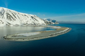 The mountainous sea coast covered with snow in a sunny weather with an old beacon on the spit.