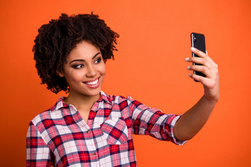 Close up photo of pretty cute lady hold hands telephone make selfies wear casual checkered plaid shirt isolated orange bright background