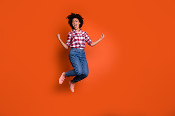 Full size photo of excited crazy jumping high lady yelling yeah raise fists wear jeans denim pants plaid shirt outfit isolated orange background