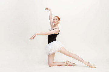 Fototapeta na wymiar Young and incredibly beautiful ballerina is posing and dancing in a light grey studio full of light. The photo greatly reflects the incomparable beauty of a classical ballet art. Copy space