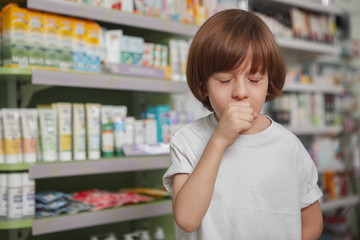 Little sick boy coughing at the drugstore, copy space. Ill young boy suffering from seasonal flu