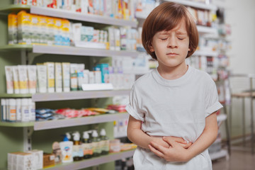 Little boy having terrible stomach ache, holding his belly with eyes closed in pain, copy space. Poor little child suffering from abdominal pain
