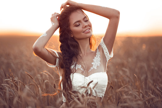 Boho chic style. Portrait of bohemian girl with white art posing over wheat field enjoying at sunset. Outdoors photo. Tranquility concept. Lifestyle.