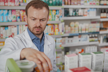 Close up of a mature male pharmacist looking concentrated, organizing medical products on shelves, copy space