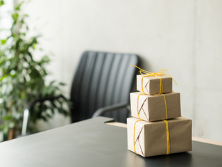 Goods delivery service. Closeup of beige paper wrapped gift boxes stack on office desk. Copy space.