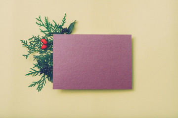 Festive greeting card. Purple mockup paper sheet with green juniper sprig and fall berries decor on beige background. Copy space.