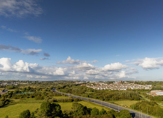 Residential areas on each side of a road and fields, aerial view, Galway, cloudy sky, sunny day.
