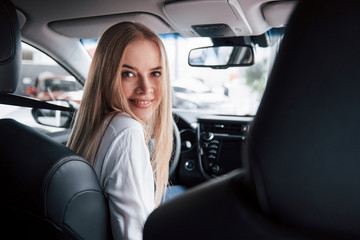 Fototapeta na wymiar Sincere smile. Beautiful blonde girl sitting in the new car with modern black interior