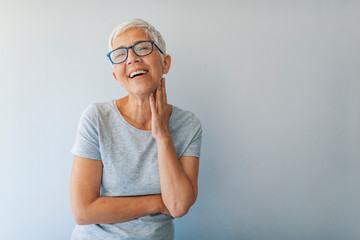 Beautiful senior woman in front of grey background.  Portrait of business woman with glasses smiling. Happy senior woman. Isolated. Portrait of mature woman with eyeglasses on grey background