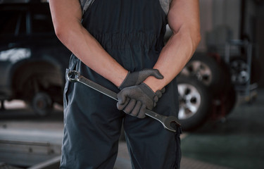 Mechanic looks forward. Rear view of worker in uniform that stands in workshop with wrench in hand