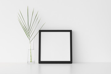 Black square frame mockup with palm leaf in a glass vase.