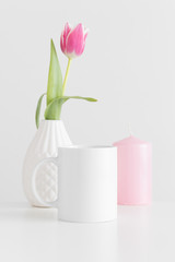 Mug mockup with a pink tulip in a vase and candle on a white table.