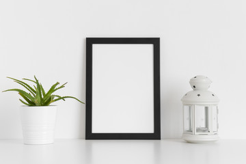 Black frame mockup with a succulent plant and a candle holder on a white table. Portrait orientation.