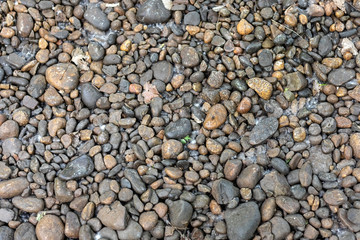 Round brown stones on the bottom of a dried-up creek in the city park.