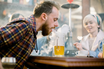 Large group multiethnical friends boys and girls sitting at table in cafe, drinking beer and smoking hookah.