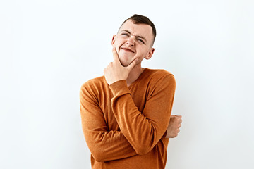  Thoughtful, thinking,dreamlike emotion concept. Young man in orange color sweater,face portrait on white backgound.