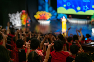 Children excitingly raise hands watching the performance in the theater - obrazy, fototapety, plakaty