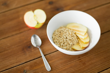 food, breakfast and healthy eating concept - oatmeal in bowl with sliced apple and spoon on wooden table