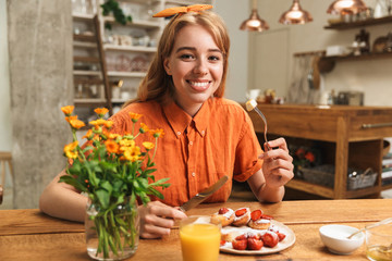 Happy young blonde girl at the kitchen eat sweet pastry have a breakfast drinking juice.