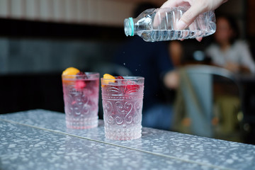 Woman's hand holding a bottle of water Pouring water into a glass with mix berries top. selective focus.
