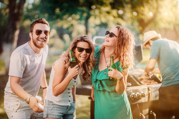 Group of friends having drinks and cooking at barbecue party