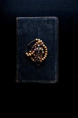 Rosary beads and prayer book on dark background.