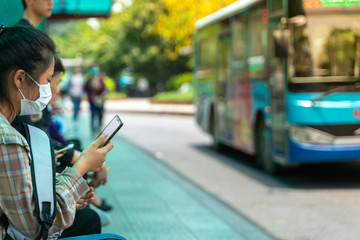 Asian young girl use smartphone waiting for bus at bus stop