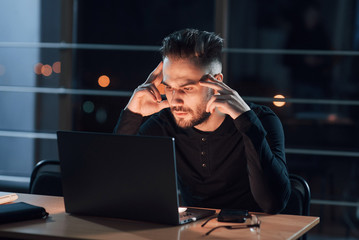 Tired look. Stylish young businessman works alone in the office at nightime