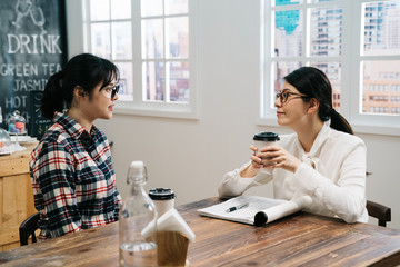 asian woman company leader listening reviewing female job applicant after reading resume CV. job interview in cafe shop. friendly hiring manager smiling drinking coffee while candidate talking.