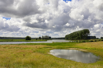 Landscape in Flanders with river, lake, meadows, trees under a dramatic sky