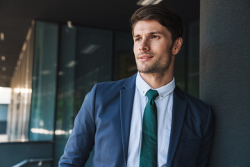 Fototapeta premium Concentrated serious young unshaved handsome business man outdoors at the street near business center posing looking aside.