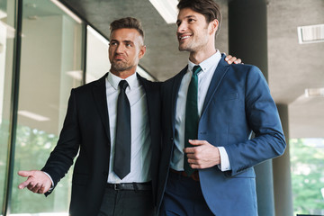 Portrait of two joyful businessmen partners walking outside job center during working meeting