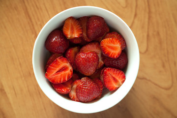Fresh strawberries in a bowl on wooden table with low key scene.
