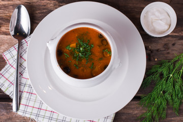 Traditional Russian meat soup Solyanka in bowl on rustic wooden table.