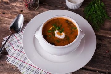 Traditional Russian meat soup Solyanka in bowl on rustic wooden table.