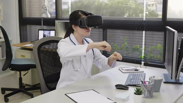 slow motion doctor woman watching computed tomography shot using vr headset sitting at desk in hospital office. female medical nurse staff intern practicing doing surgery wear virtual reality glasses