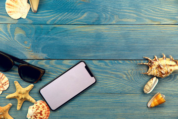 Background. On the blue wooden background on the left are sunglasses, a telephone and different shells, on the right are three seashells. A free space in the center, horizontal. Tourism concept.