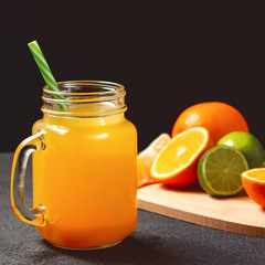 Naklejka na ściany i meble Freshly made citrus juice from oranges, grapefruit and lime in a jar-mug with a straw on black table