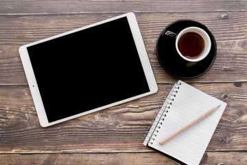 An overhead view of digital tablet; coffee cup and spiral notebook with pencil on wooden textured table