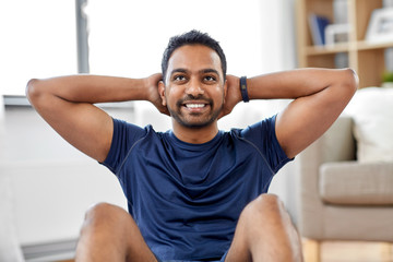 sport, fitness and healthy lifestyle concept - smiling indian man making abdominal exercises at home