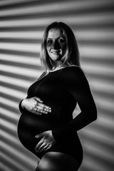 A pregnant woman in lingerie with a big belly in the ninth month of pregnancy is posing next to a...