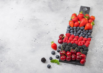 Naklejka na ściany i meble Fresh organic summer berries mix on black marble board on light kitchen table background. Raspberries, strawberries, blueberries, blackberries and cherries. Space for text