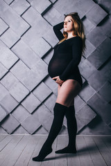 A pregnant woman in lingerie with a big belly in the ninth month of pregnancy is posing next to a...
