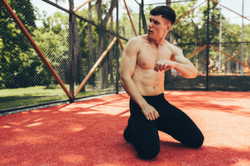 Obraz premium Handsome fit male taking a rest after training session outdoors. Healthy athlete man sitting at pavement sportsground and realxing after workout exercises. People and sport concept