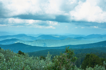 The ridge of mountains covered with forest is under a cloudy sky.