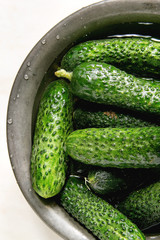 Fresh ripe organic garden cucumbers in metal bowl over white marble background. Flat lay, close up
