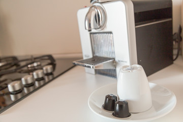 Detail of a kitchen.  White coffe cups, coffee capsules and coffee maker.  Breakfast concept